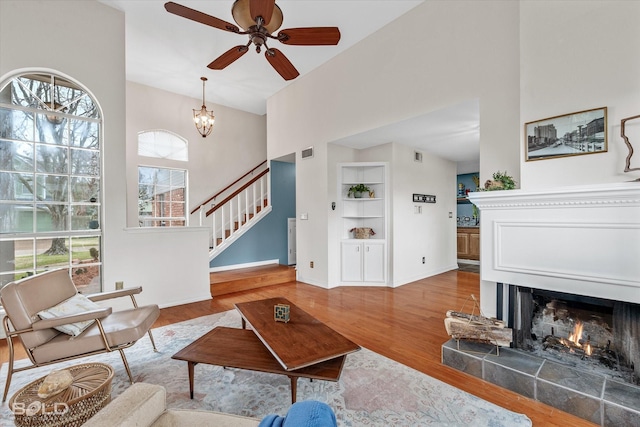 living room with a fireplace, ceiling fan with notable chandelier, wood-type flooring, and built in shelves