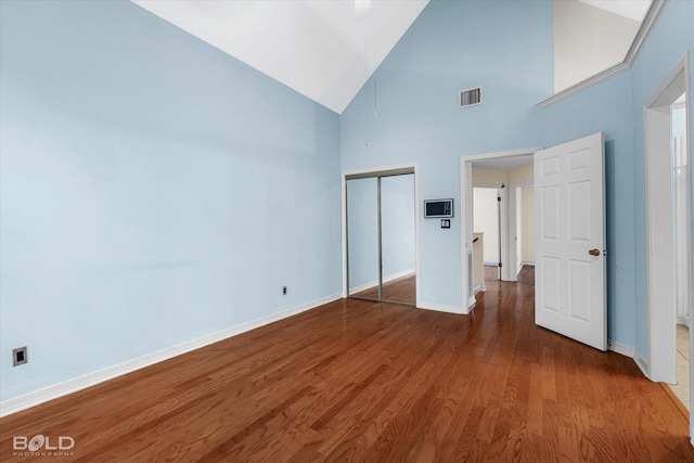 unfurnished bedroom featuring high vaulted ceiling, hardwood / wood-style floors, and a closet