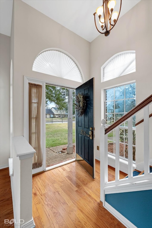 foyer featuring a towering ceiling, wood-type flooring, and a notable chandelier