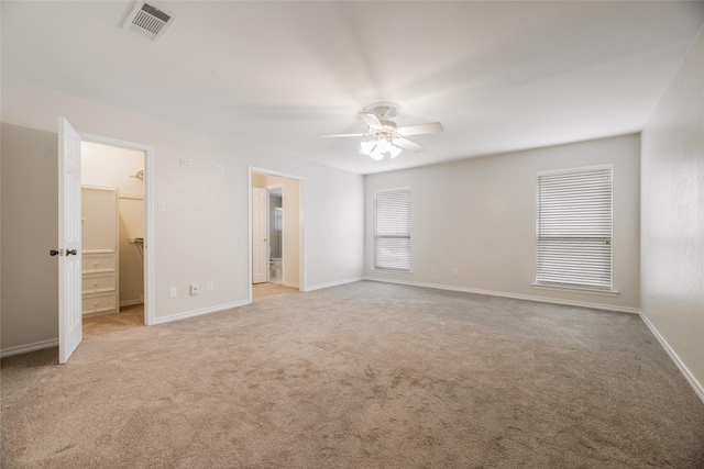 unfurnished bedroom with a spacious closet, ensuite bath, a closet, ceiling fan, and light colored carpet