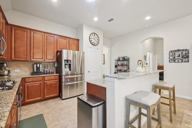 kitchen with light stone countertops, appliances with stainless steel finishes, a kitchen island, tasteful backsplash, and a breakfast bar