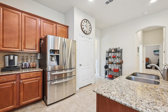 kitchen featuring sink, backsplash, stainless steel fridge with ice dispenser, and light stone counters