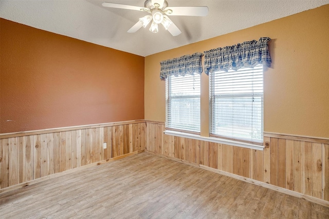 spare room featuring wood-type flooring, a textured ceiling, ceiling fan, and wood walls