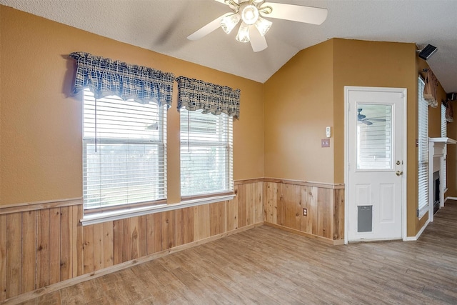 interior space featuring vaulted ceiling, wooden walls, wood-type flooring, ceiling fan, and a textured ceiling