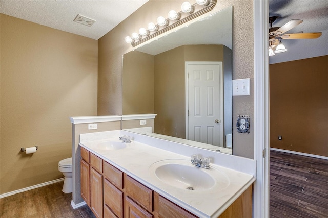 bathroom with toilet, a textured ceiling, vanity, hardwood / wood-style flooring, and ceiling fan