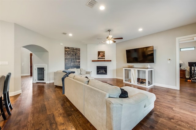 living room featuring ceiling fan, a large fireplace, and dark hardwood / wood-style floors