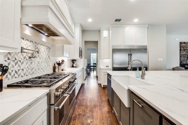 kitchen featuring built in appliances, white cabinetry, light stone countertops, and premium range hood