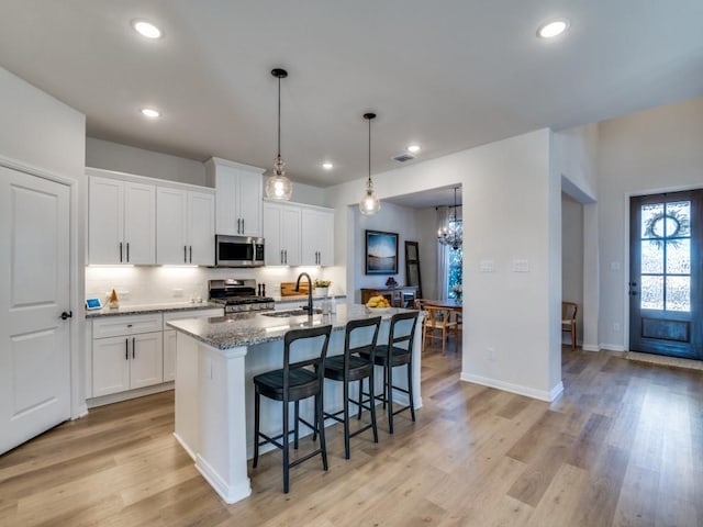 kitchen with light hardwood / wood-style flooring, white cabinetry, stainless steel appliances, an island with sink, and stone countertops