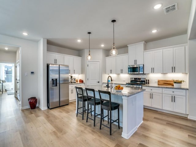 kitchen with appliances with stainless steel finishes, white cabinets, decorative backsplash, light stone countertops, and a center island with sink