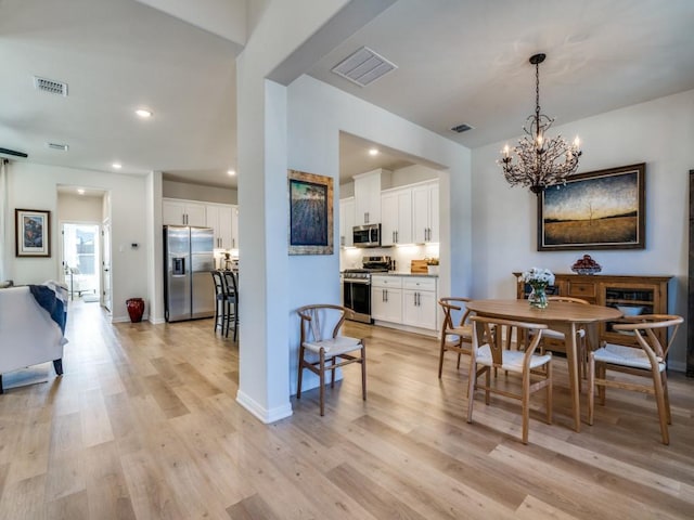 dining space with a chandelier, light wood finished floors, and visible vents