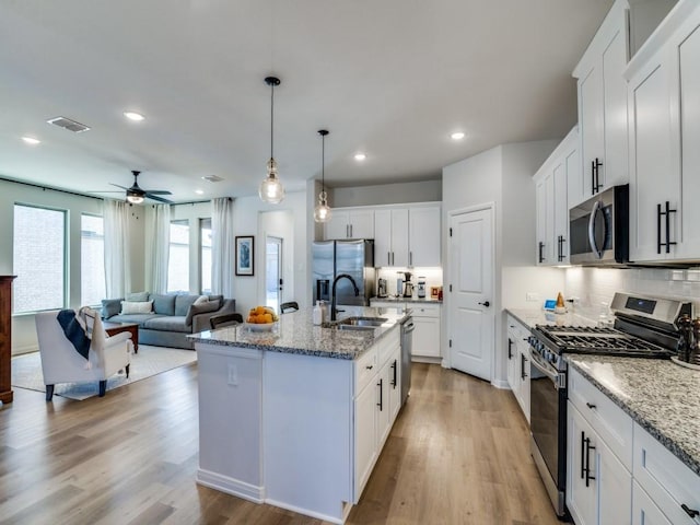 kitchen with appliances with stainless steel finishes, pendant lighting, white cabinetry, light stone countertops, and a center island with sink