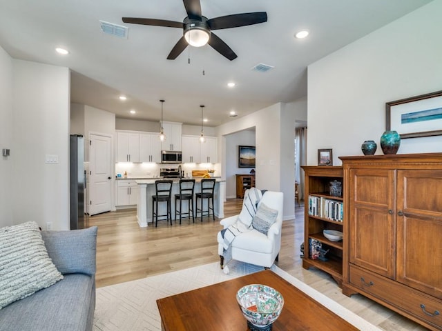 living room featuring light wood-style floors, a ceiling fan, visible vents, and recessed lighting