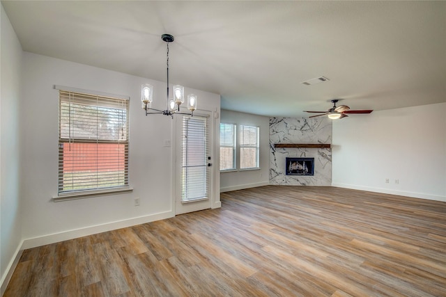 unfurnished living room with hardwood / wood-style floors, ceiling fan with notable chandelier, and a fireplace