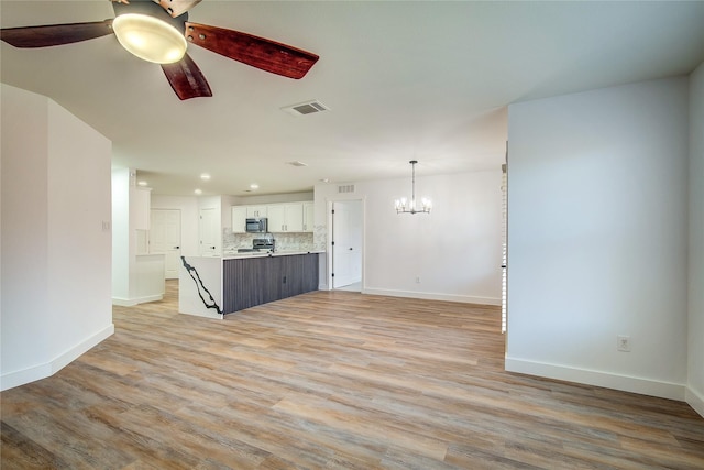 unfurnished living room featuring ceiling fan with notable chandelier and light wood-type flooring