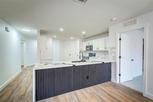 kitchen featuring white cabinetry, kitchen peninsula, decorative backsplash, and light hardwood / wood-style flooring