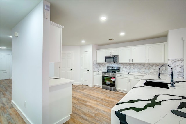 kitchen featuring appliances with stainless steel finishes, tasteful backsplash, white cabinetry, sink, and light wood-type flooring