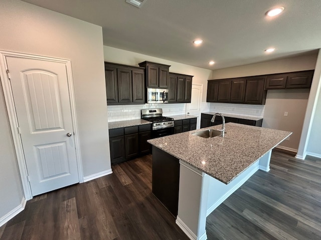 kitchen with dark wood-type flooring, light stone counters, stainless steel appliances, and a sink