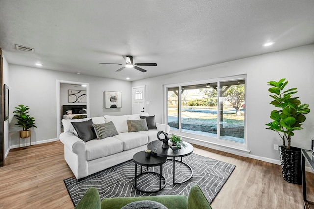 living room with light wood-type flooring, ceiling fan, and a textured ceiling