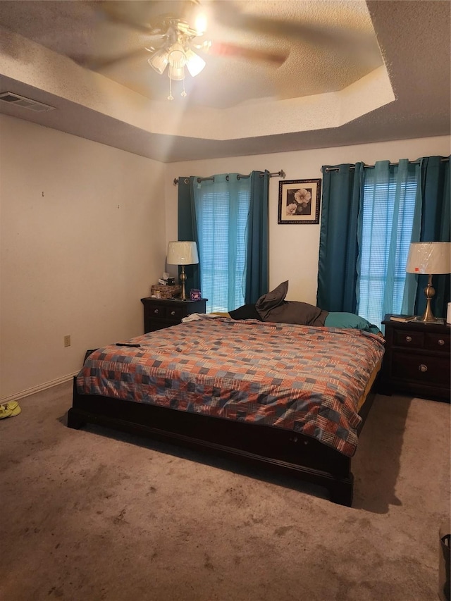 bedroom with a textured ceiling, ceiling fan, carpet, and a tray ceiling