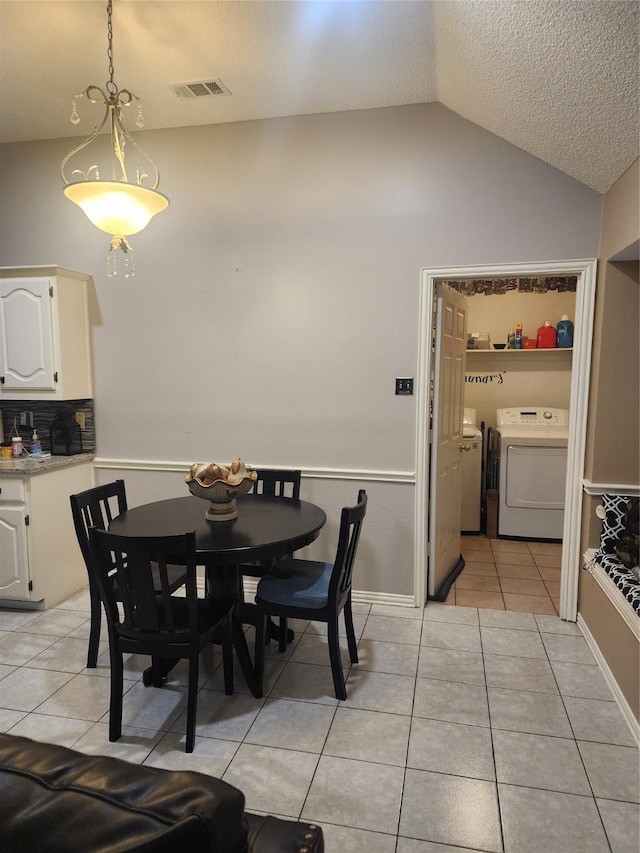 dining room featuring washing machine and clothes dryer, vaulted ceiling, a textured ceiling, and light tile patterned flooring