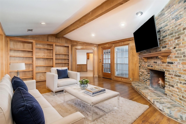 living room with light hardwood / wood-style floors, a brick fireplace, wood walls, and lofted ceiling with beams