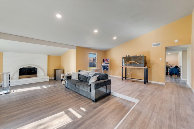 living room with a brick fireplace, light hardwood / wood-style flooring, and lofted ceiling