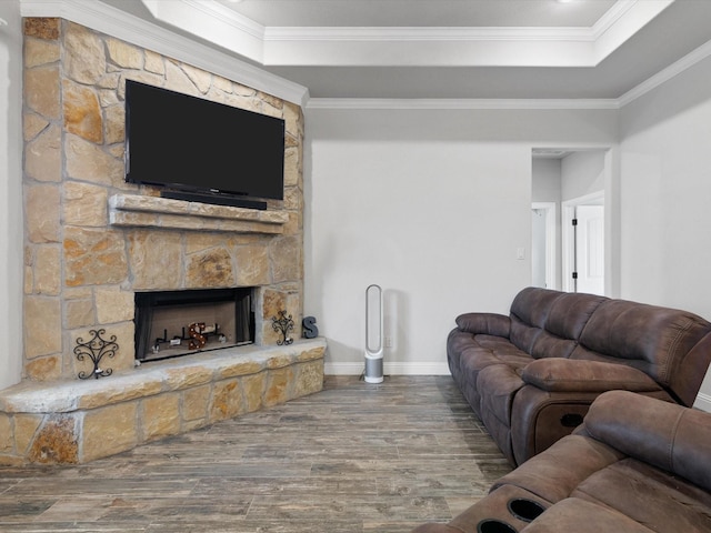 living room with a raised ceiling, a stone fireplace, ornamental molding, and hardwood / wood-style floors