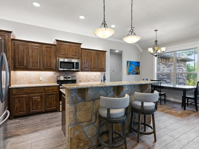 kitchen featuring decorative light fixtures, a kitchen island with sink, tasteful backsplash, and stainless steel appliances