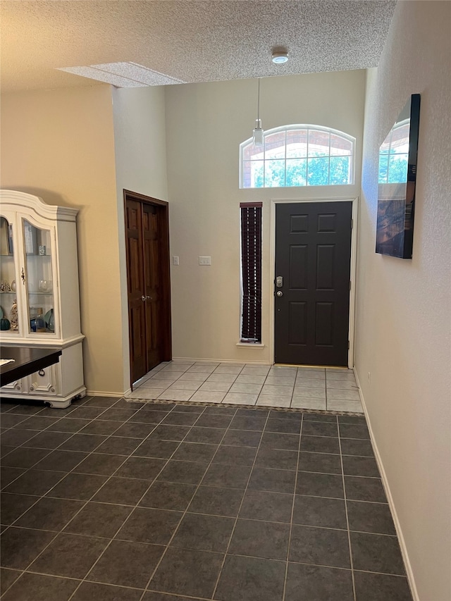 foyer with a high ceiling, a textured ceiling, and dark tile patterned floors