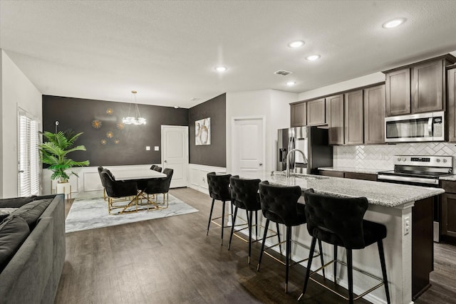 kitchen with dark brown cabinetry, a kitchen bar, stainless steel appliances, sink, and a center island with sink