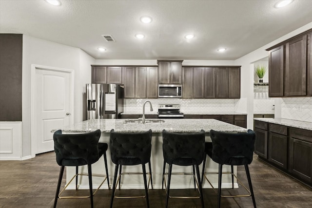 kitchen with appliances with stainless steel finishes, dark hardwood / wood-style flooring, a center island with sink, and sink