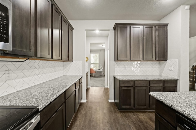 kitchen featuring a textured ceiling, dark brown cabinetry, dark wood-type flooring, tasteful backsplash, and light stone counters