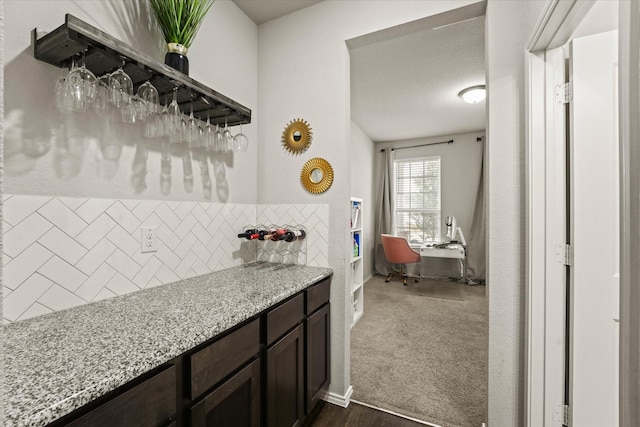 interior space featuring dark colored carpet, backsplash, light stone countertops, and dark brown cabinets