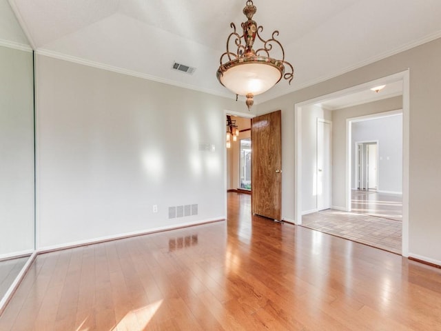 empty room featuring vaulted ceiling, ornamental molding, and hardwood / wood-style floors