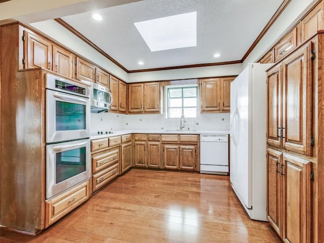 kitchen featuring a skylight, stainless steel appliances, light hardwood / wood-style floors, sink, and crown molding