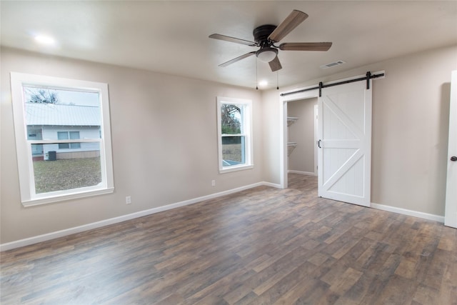 unfurnished bedroom featuring a spacious closet, dark hardwood / wood-style floors, a closet, ceiling fan, and a barn door