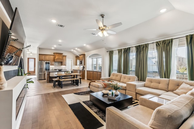 living room with ceiling fan, light hardwood / wood-style flooring, and vaulted ceiling