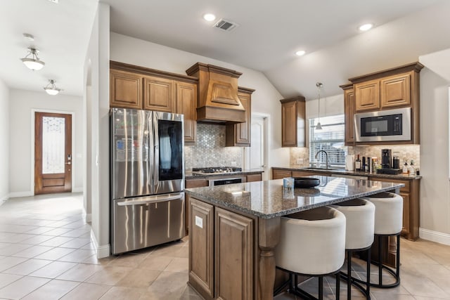 kitchen featuring appliances with stainless steel finishes, light tile patterned flooring, dark stone counters, pendant lighting, and a center island