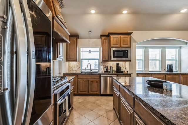 kitchen with dark stone countertops, a wealth of natural light, sink, stainless steel appliances, and light tile patterned floors