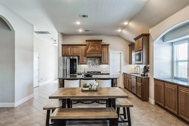 kitchen featuring appliances with stainless steel finishes, wall chimney range hood, dark stone countertops, and a center island