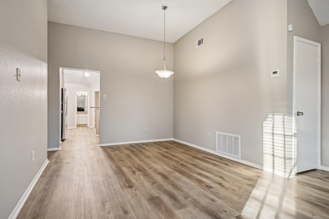 empty room featuring high vaulted ceiling, a textured ceiling, and hardwood / wood-style flooring