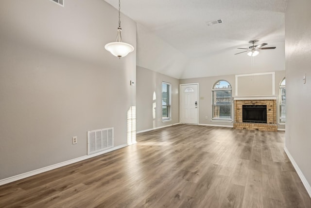 unfurnished living room with ceiling fan, vaulted ceiling, a brick fireplace, and wood-type flooring