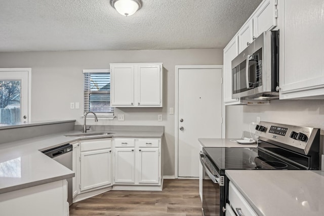 kitchen featuring appliances with stainless steel finishes, wood-type flooring, a textured ceiling, white cabinets, and sink