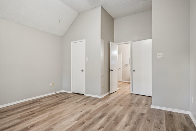 unfurnished bedroom with light wood-type flooring, a textured ceiling, and high vaulted ceiling