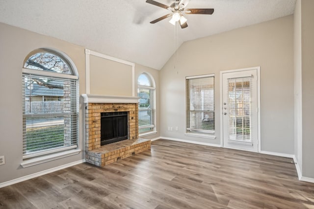 unfurnished living room featuring ceiling fan, a brick fireplace, a wealth of natural light, and lofted ceiling