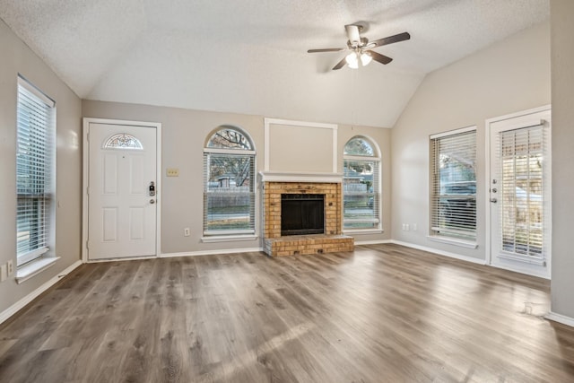 unfurnished living room with hardwood / wood-style floors, lofted ceiling, a fireplace, plenty of natural light, and ceiling fan