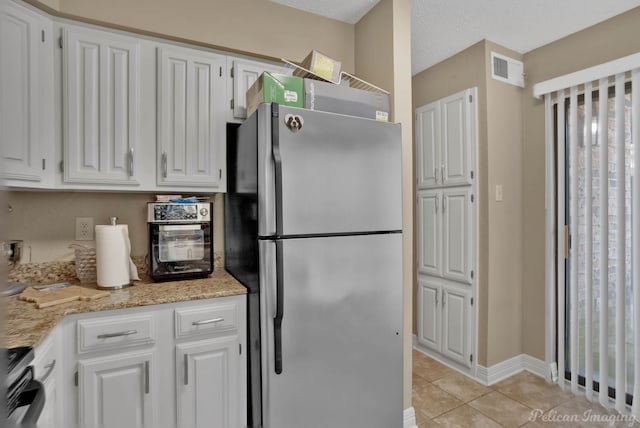 kitchen featuring light tile patterned floors, stainless steel fridge, light stone countertops, range, and white cabinets