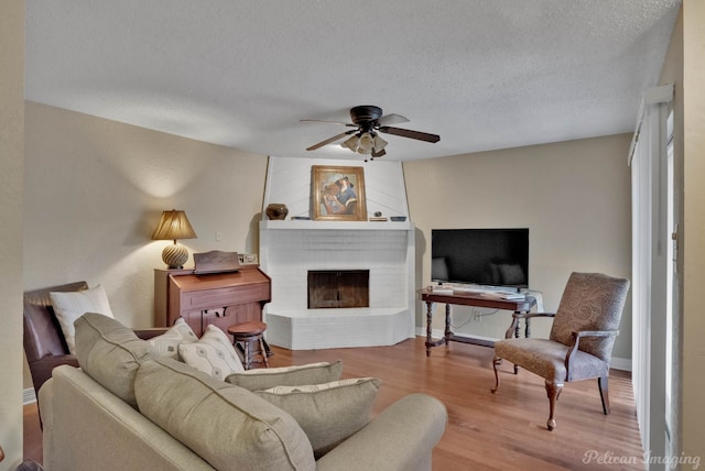 living room with ceiling fan, a textured ceiling, light hardwood / wood-style flooring, and a fireplace