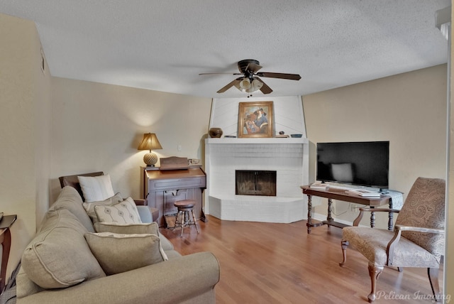 living room with ceiling fan, hardwood / wood-style floors, a textured ceiling, and a fireplace