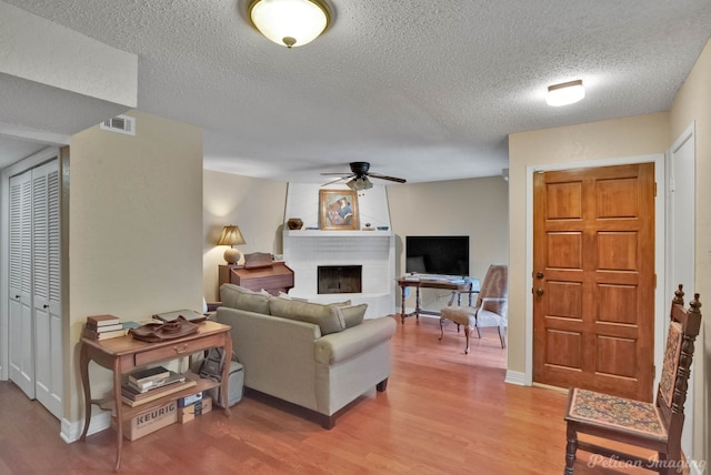 living room featuring ceiling fan, a textured ceiling, hardwood / wood-style floors, and a fireplace